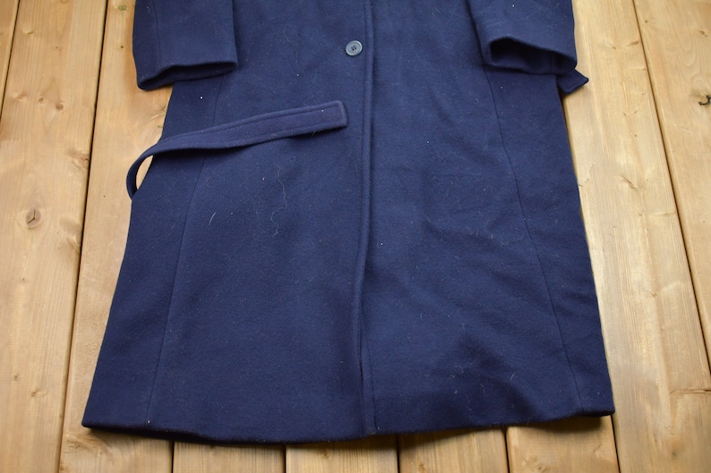 Pu&ograve; includere: Un cappotto di lana blu navy con una chiusura a bottone singolo e una cintura. Il cappotto ha un design classico ed &egrave; in buone condizioni.