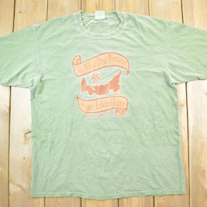 May include: A green t-shirt with a faded orange print of a dog paw print and the text "No Three Dogs Fence Prince Edward Island".