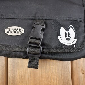Op de afbeelding: Zwarte canvas tas met een Mickey Mouse-patch en een zilveren metalen label met de tekst "Classic Mickey".