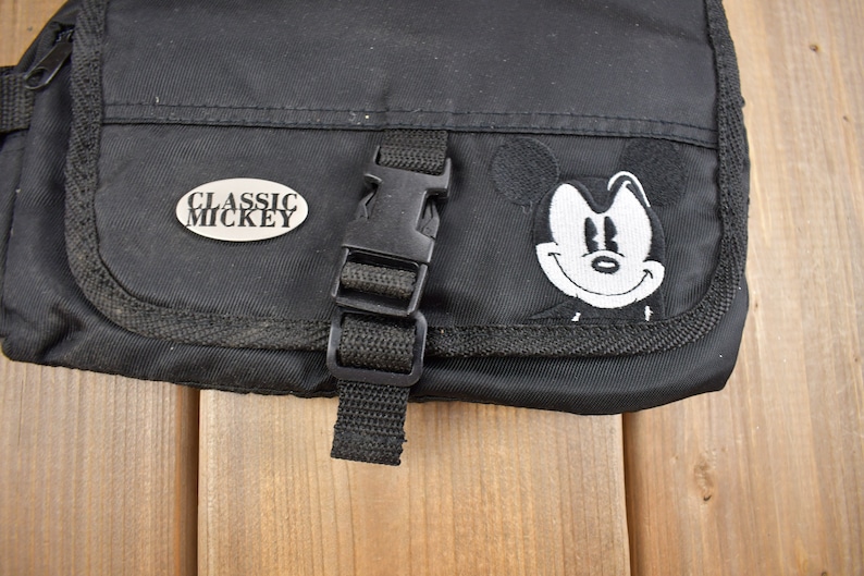 Op de afbeelding: Zwarte canvas tas met een Mickey Mouse-patch en een zilveren metalen label met de tekst "Classic Mickey".