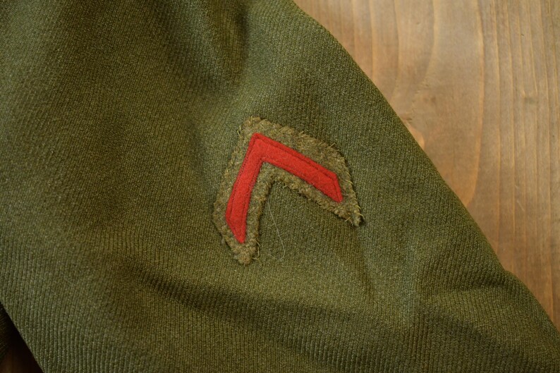 May include: A green military uniform with a red chevron patch sewn on the sleeve.