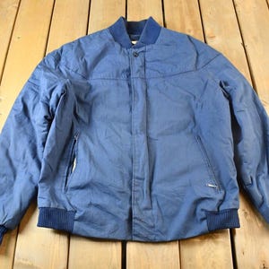 Pode incluir: Uma jaqueta de brim azul com fecho de correr e gola e punhos canelados.