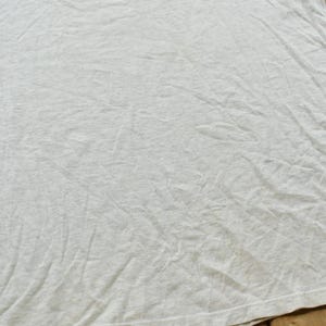 Op de afbeelding: Een lichtgrijs t-shirt met korte mouwen en een subtiele gespikkelde textuur door de hele stof. Het kledingstuk heeft een ronde halslijn en een standaard zoom, met een effen, onbedrukt oppervlak met zichtbare vouwen en kreukels in de stof.