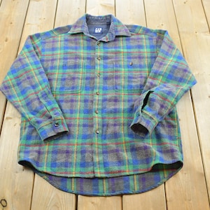 May include: A long-sleeve button-up shirt featuring a plaid pattern in shades of blue, green, and yellow. The shirt has a collar, two chest pockets with button closures, and a buttoned front placket. The interior label reads Gap.