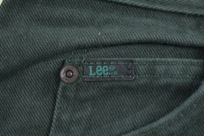 May include: Close-up of a dark green pair of pants with a black Lee&reg; label sewn on the back pocket.