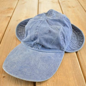 May include: A light blue, vintage-style hat with a brim and ear flaps. The hat is made of a soft, faded fabric and has a classic, worn look. The brim is curved, and the ear flaps provide extra coverage. This hat is perfect for outdoor activities.