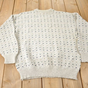 May include: A cream-coloured sweater with a diamond pattern in navy blue and gold.