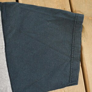 May include: Close-up of a two-tone t-shirt sleeve. The sleeve is divided into two sections: a light gray panel and a dark navy blue panel. The edge of the sleeve is hemmed with a visible seam.