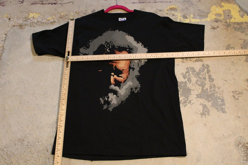 May include: Black t-shirt with a graphic print of a person's face in shades of gray and brown.