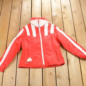 May include: A red ski jacket with white stripes down the sleeves and across the chest. The jacket has a zipper closure and a hood.