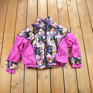 Puede incluir: Una chaqueta de color rosa y negro con estampado floral y cierre de cremallera. La chaqueta tiene un cuello alto y mangas largas.