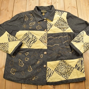 May include: A denim jacket with a patchwork design featuring animal prints in shades of brown, black, and yellow. The jacket has a button-up closure and long sleeves.