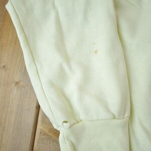 May include: A pale yellow sweatshirt with a small brown stain on the front. The sweatshirt has long sleeves and a ribbed cuff.
