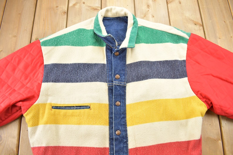May include: A striped denim jacket with red quilted sleeves. The jacket has a white, green, blue, yellow, and red striped pattern. The jacket has a button closure and a pocket on the left side.