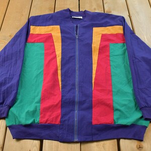 Peut inclure: Une veste zippée à manches longues présentant un design color-block vibrant en violet, vert, rouge et orange. La veste possède une fermeture éclair centrale, un col côtelé et des poignets côtelés, avec des panneaux de couleur verticaux.