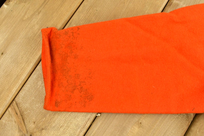 K&ouml;nnte beinhalten: Nahaufnahme des orangenen Stoff&auml;rmels eines Kleidungsst&uuml;cks. Der Stoff hat eine strukturierte, leicht abgenutzte Optik mit braunen Flecken.