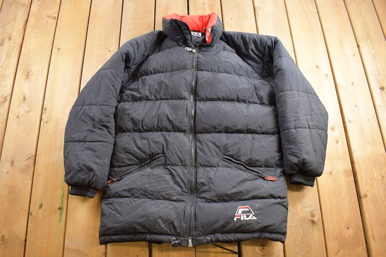 May include: Black puffer jacket with a red and white inner collar and a Fila logo on the bottom left side.