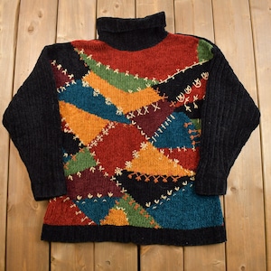 以下が含まれることがあります： カラフルなパッチワークのデザインが施された、黒いタートルネックセーター。セーターは、赤、オレンジ、黄色、緑、青、茶色など、さまざまな色を使用しています。パッチワークのデザインは、コントラストのある糸で縫い合わされています。