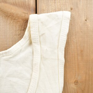 May include: A white sleeveless shirt with a plain design. The shirt is made of a soft, lightweight fabric.