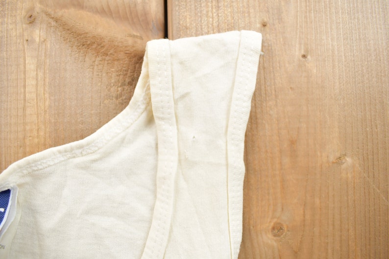 May include: A white sleeveless shirt with a plain design. The shirt is made of a soft, lightweight fabric.
