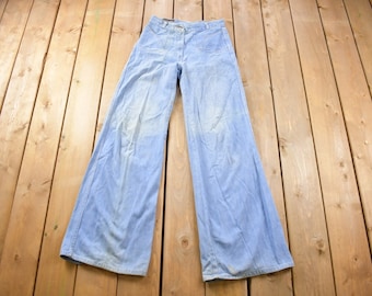 Può includere: Un paio di pantaloni a campana in denim blu chiaro. I pantaloni hanno la vita alta e sono realizzati in un tessuto morbido e confortevole.