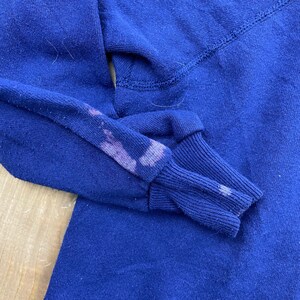 Op de afbeelding: Een close-up van een marineblauw longsleeve shirt met een vervaagde paarse vlek op de mouw.