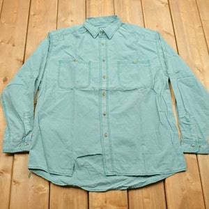 May include: A light blue long-sleeved button-down shirt with two chest pockets and a button-up front.