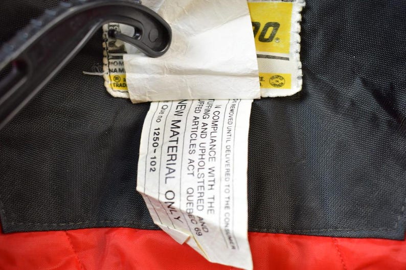 May include: A white tag with black text that reads "NEW MATERIAL ONLY" and "Que no 1250-102". The tag is attached to a black fabric with a yellow tag that reads "WOW" in black text.