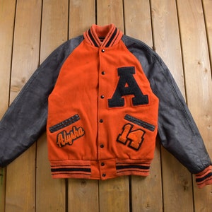 Könnte beinhalten: Eine rote und schwarze Varsity-Jacke mit Lederärmeln. Die Jacke hat ein großes "A" auf der Vorderseite, eine "14" auf der rechten Seite und den Namen "Alysha" auf der linken Seite.