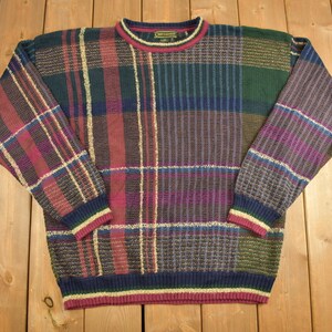 May include: A multi-coloured plaid jumper with a crew neck and long sleeves. The jumper is made of a soft, knitted fabric and features a variety of colours, including red, green, blue, and purple.