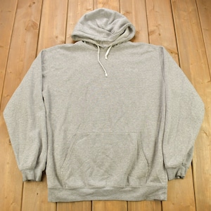 Puede incluir: Una sudadera con capucha gris con un bolsillo canguro en la parte delantera. La sudadera tiene una capucha con cord&oacute;n y un peque&ntilde;o logotipo en la parte delantera.