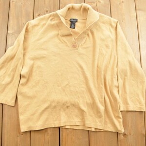May include: A light brown, long-sleeved sweater with a mock neck and a single button closure. The sweater is made of a soft, knitted fabric.