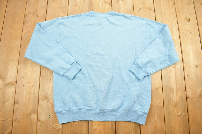 May include: A light blue sweatshirt with long sleeves and a crew neck.