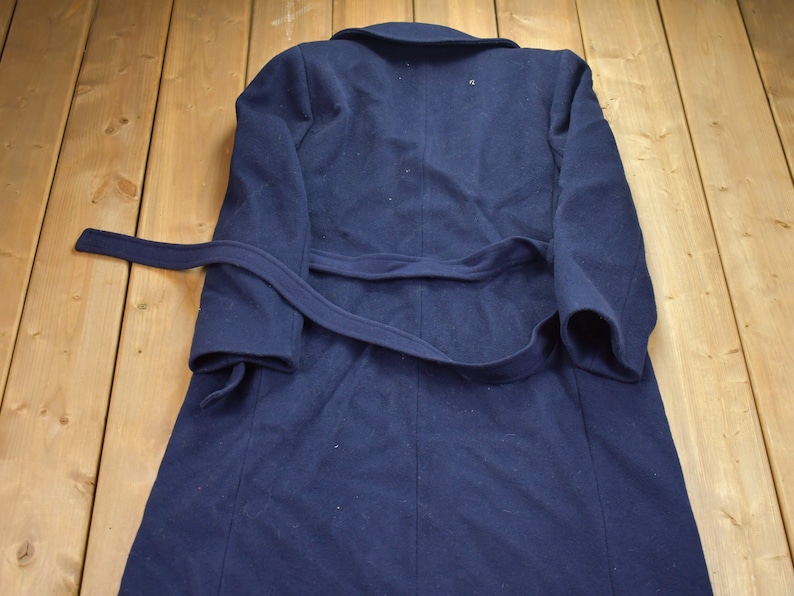 Pu&ograve; includere: Un cappotto di lana blu navy con cintura da annodare. Il cappotto ha un design classico ed &egrave; perfetto per il clima freddo.