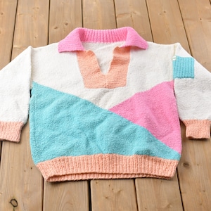 May include: A white, pink and turquoise knitted jumper with a contrasting collar and a geometric design.
