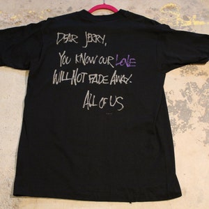 May include: Black t-shirt with a white inscription that reads "Dear Jerry, You know our love will not fade away. All of us."