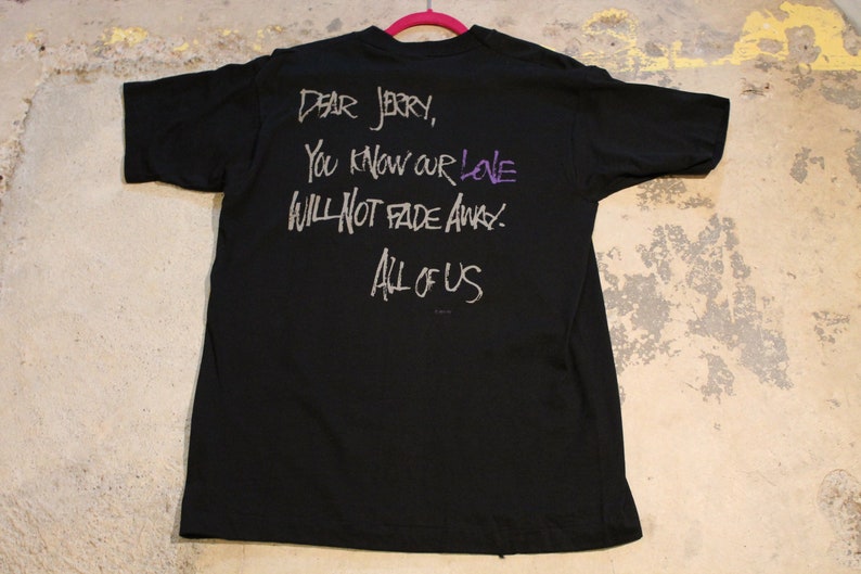 May include: Black t-shirt with a white inscription that reads "Dear Jerry, You know our love will not fade away. All of us."