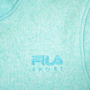 May include: Close-up of a light teal knit jacket with a full zipper. The jacket features the embroidered FILA SPORT logo in a matching teal color. The knit fabric has a speckled appearance.