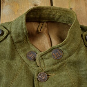 May include: A green wool jacket with a high collar and four metal buttons. The buttons have the letters "US" and "III" on them.