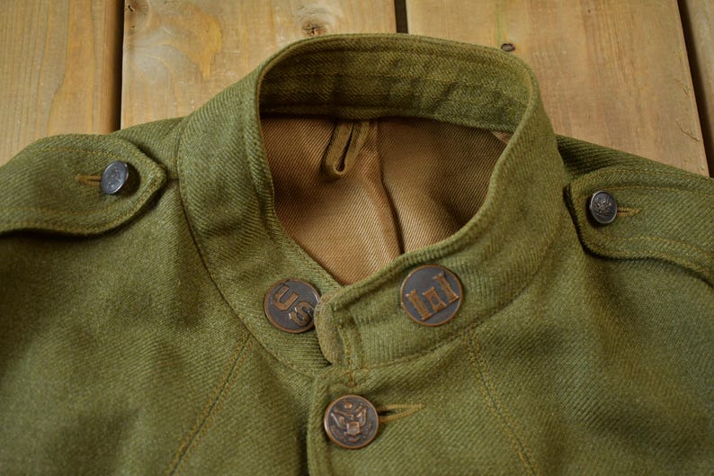 May include: A green wool jacket with a high collar and four metal buttons. The buttons have the letters "US" and "III" on them.