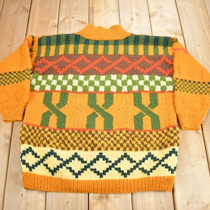 May include: A colourful knitted jumper with a geometric pattern in shades of orange, green, brown, and yellow.