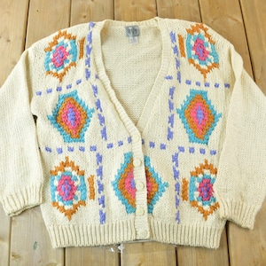 May include: A cream knitted cardigan with a geometric pattern in shades of orange, pink, blue, and purple. The cardigan has a V-neck and a button closure.