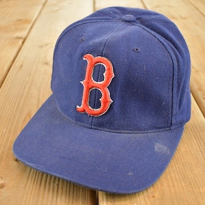 Puede incluir: Gorra de béisbol azul con el logotipo "B" rojo en la parte delantera. La gorra tiene una visera curva y un botón en la parte superior. El sombrero está hecho de tela duradera y es probablemente vintage.