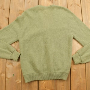 May include: A green knitted cardigan sweater with a v-neck and long sleeves.