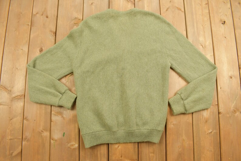 May include: A green knitted cardigan sweater with a v-neck and long sleeves.