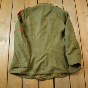 May include: A green military jacket with red trim on the sleeves. The jacket has a button closure and a collar.