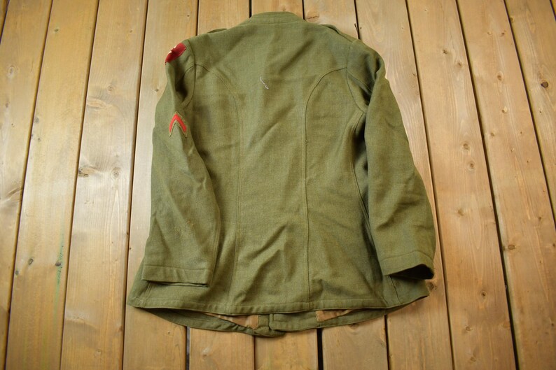 May include: A green military jacket with red trim on the sleeves. The jacket has a button closure and a collar.