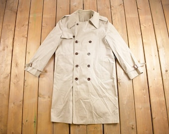 May include: A beige trench coat with a double-breasted closure and a belt. The coat has a classic design and is made of a lightweight fabric.