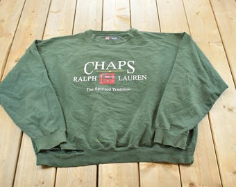 May include: Green Chaps Ralph Lauren sweatshirt with the brand name in white block letters. The sweatshirt has a crew neck and long sleeves. The text "The Spirited Tradition" is below the brand name.