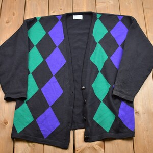 May include: A black cardigan with a diamond pattern in green and purple. The cardigan has a button closure.